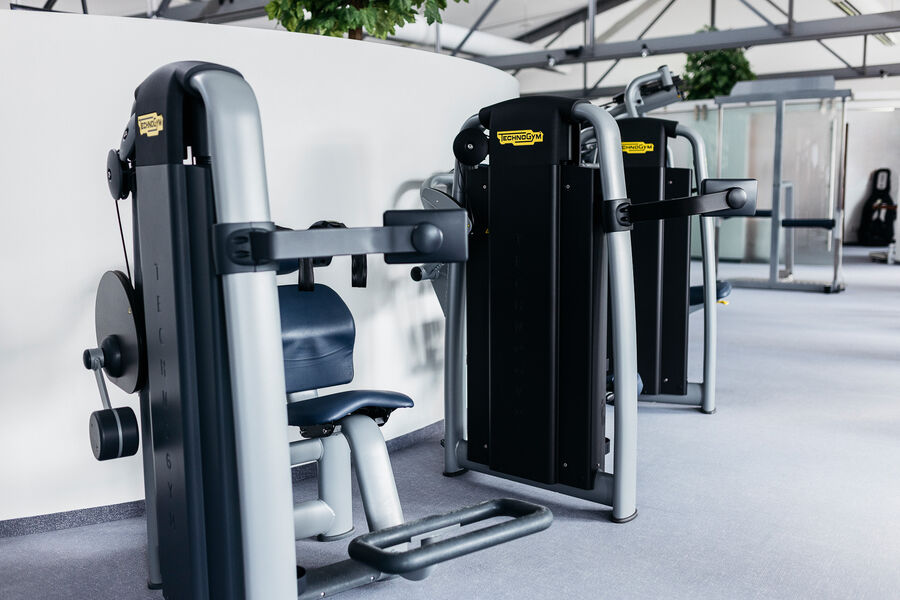 Zwei Schulter-Press-Maschinen stehen an der wand entlang in einem helem Trainingsraum.