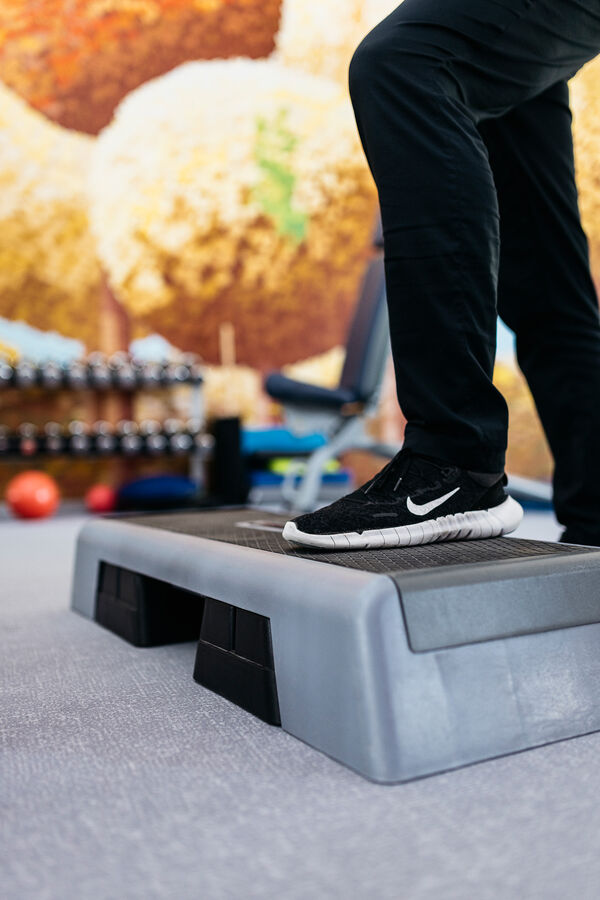 Ein Fuß in einem schwarzen Turnshcuh steht auf einem Stepper.
